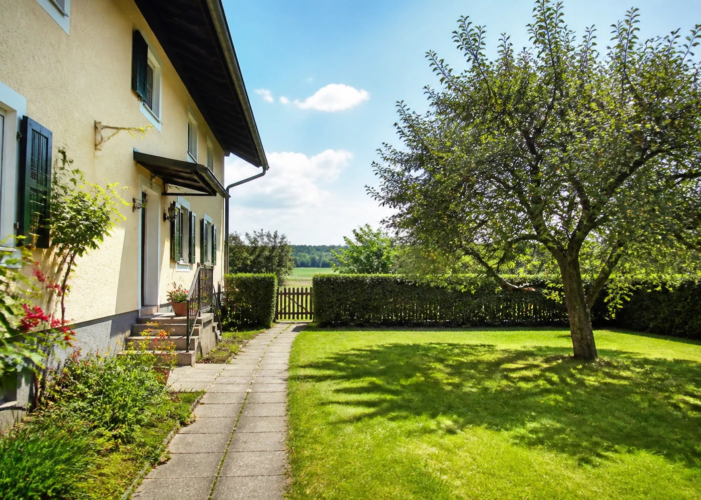 Älteres gepflegtes Wohnhaus neben hellem Gartenraum mit Obstbaum und Weg